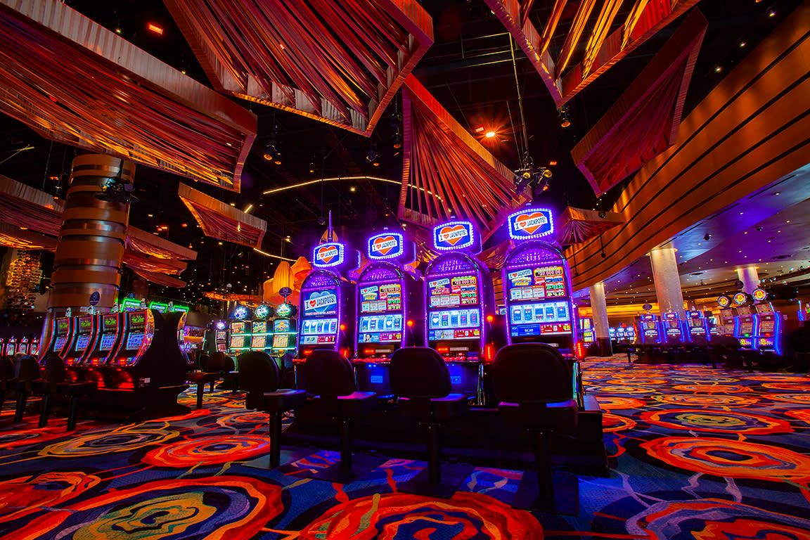 Sala de tragamonedas con carteles de jackpot iluminados en morado y naranja